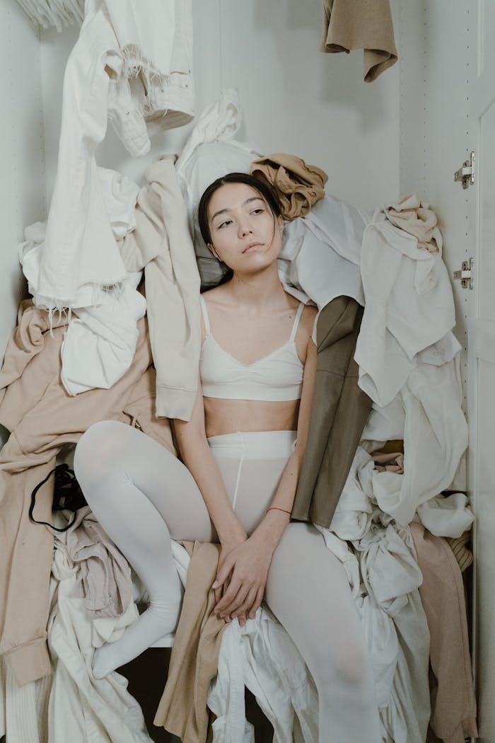 A Woman Sitting Inside the Cabinet Full of Clothes